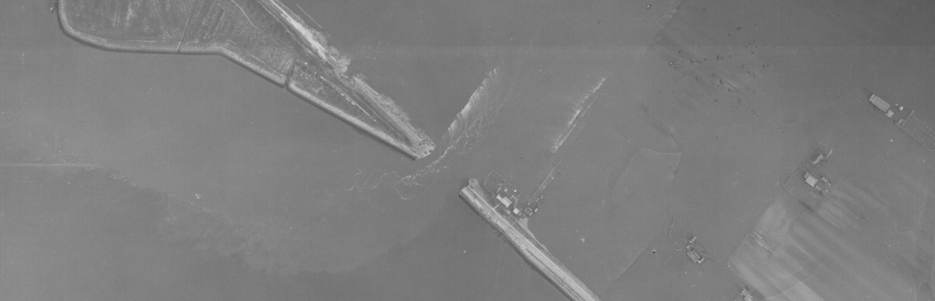 Luchtfoto uit 1953 waarin twee dijkdoorbraken zichtbaar zijn. De onderste is veranderd in een stroomgat. De bovenste ligt achter buitendijkse natuur en is niet diep uitgesleten.