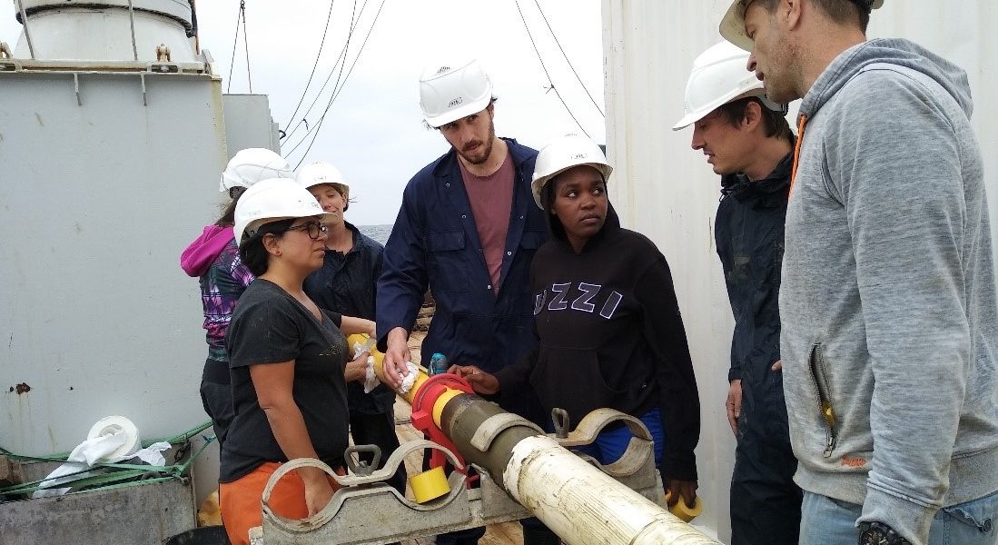 The science team on the Atlantic Ocean off Namibia, hard at work cutting the 10-m sediment core into 1-m chunks for transport and further analysis on land. Clearly very serious stuff (© Peter Kraal, NIOZ).