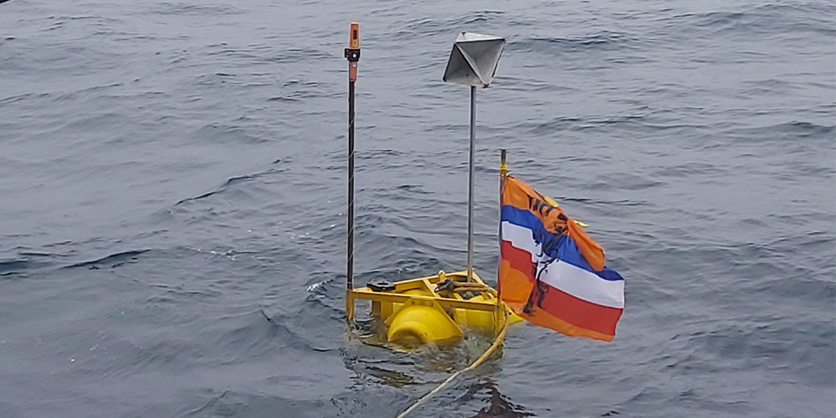 Figure 3: acoustic buoy with the Dutch flag, a radar reflector and the GPS beacon on top. The buoy was equipped with 3 acoustic recorders at 40, 80 and 120 m and a CTD sensor at the bottom (130 m)