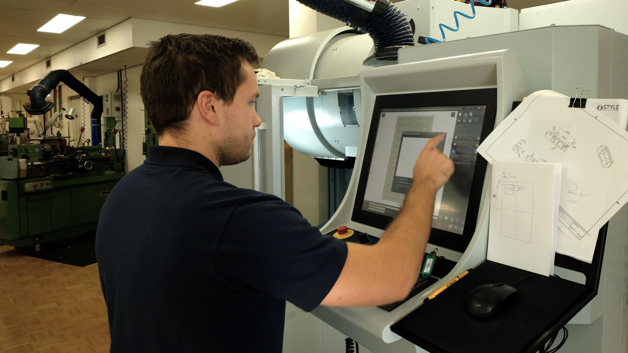 A person using a touch screen panel to set up a large milling cutter machine.