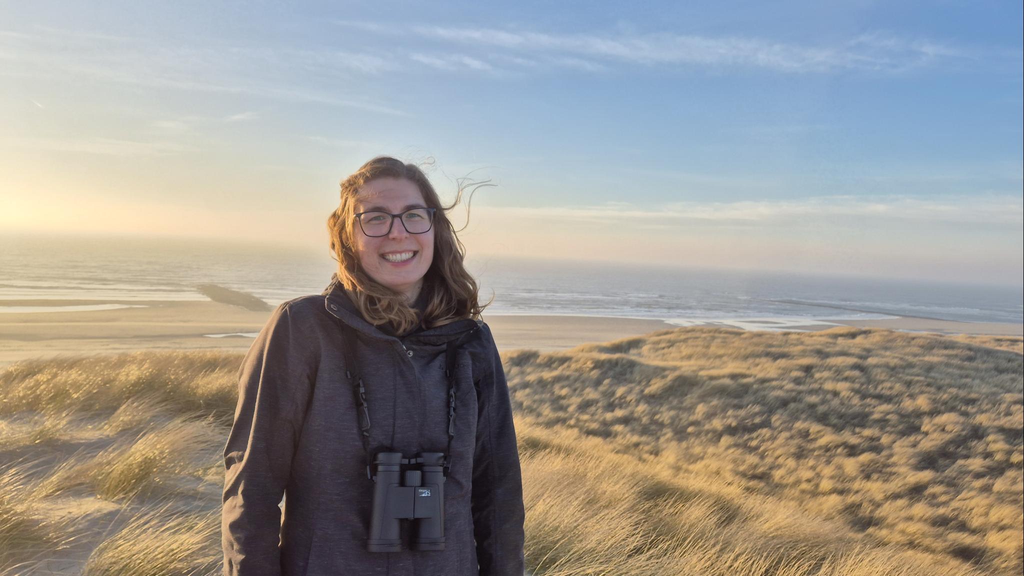 Glimlachende jonge vrouw in de duinen met zee op de achtergrond