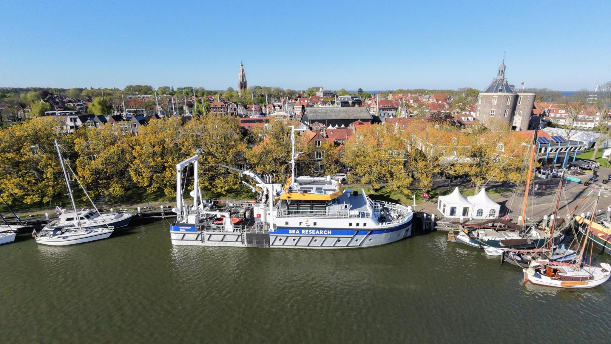 Het schip RV Wim Wolff ligt aan de kade, omringd door gewone zeilboten. In de achtergrond is de toren van Enkhuizen te zien