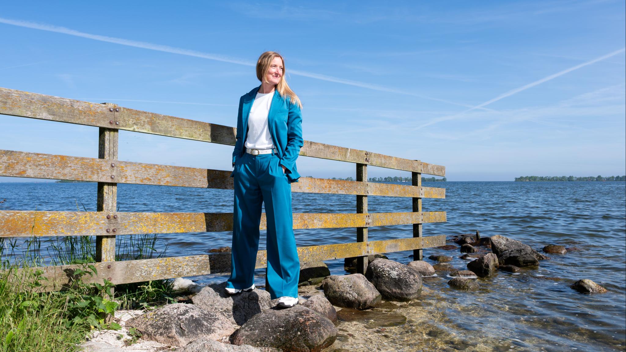 Maaike van de Kamp-Romijn staand op stenen aan de oever van een meer