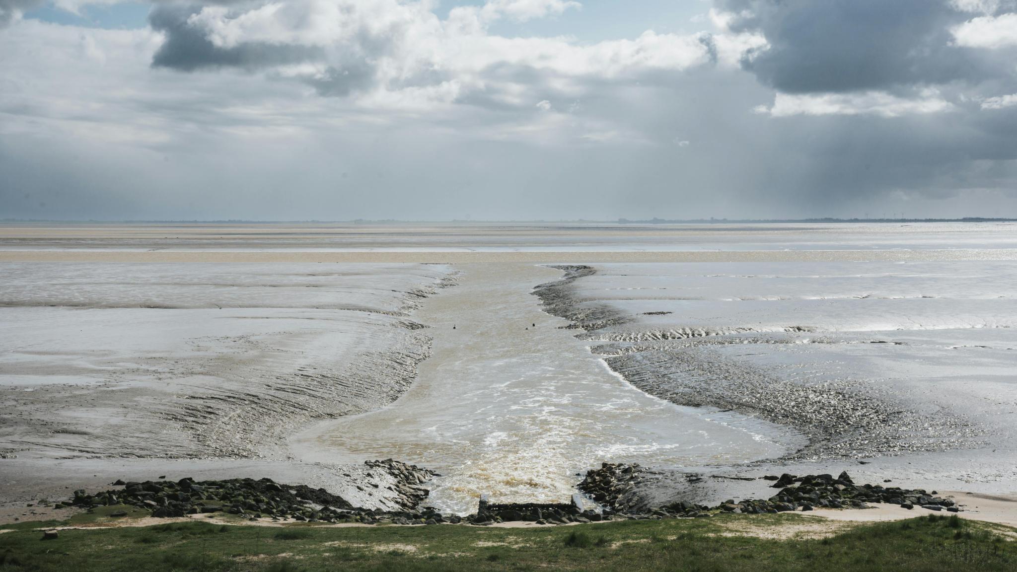 Expansive mudflats merging with the sea under dramatic clouds, showcasing nature's beauty.
