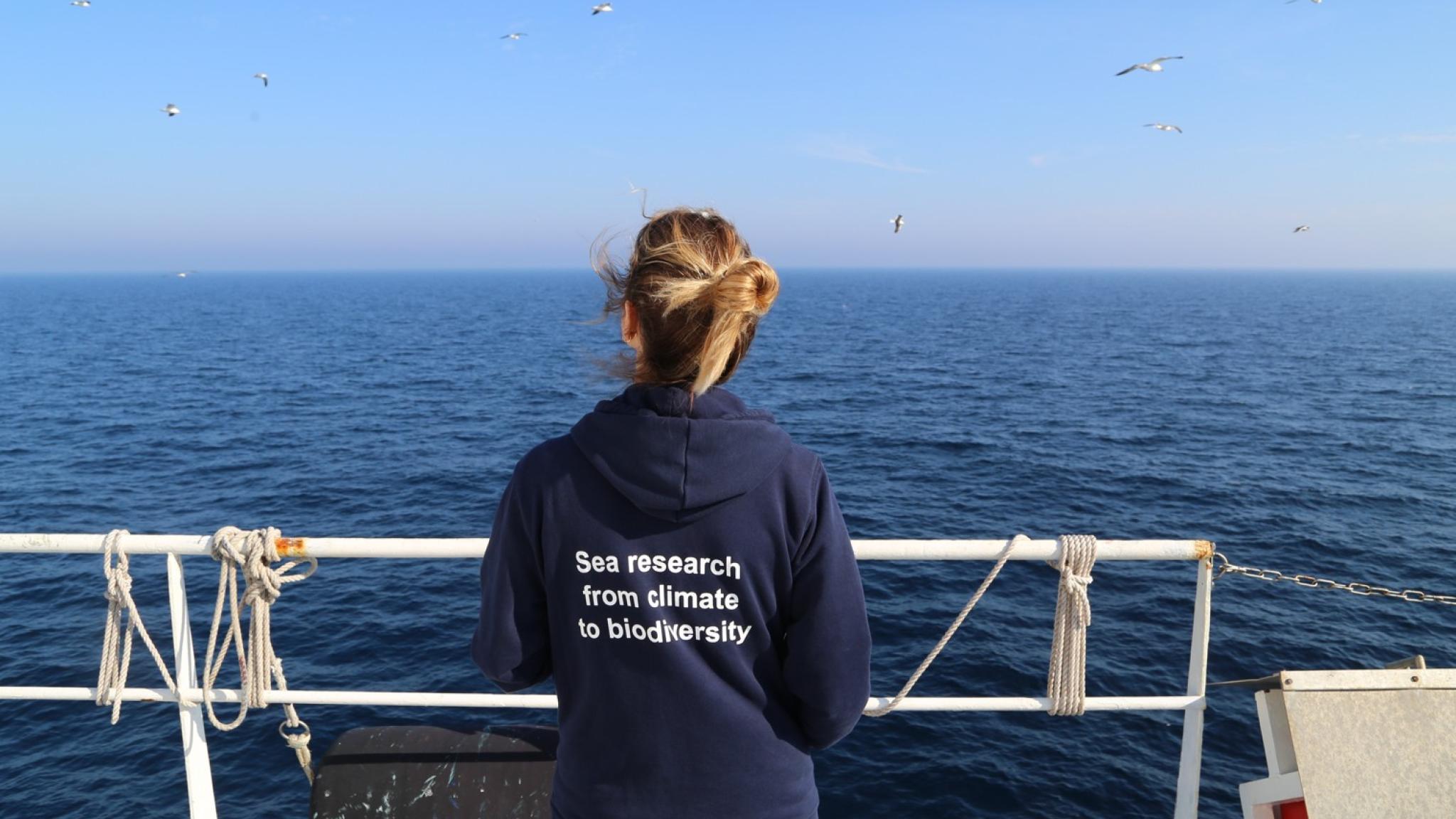 Woman seen from the back, watching the sea and holding the railing of a ship