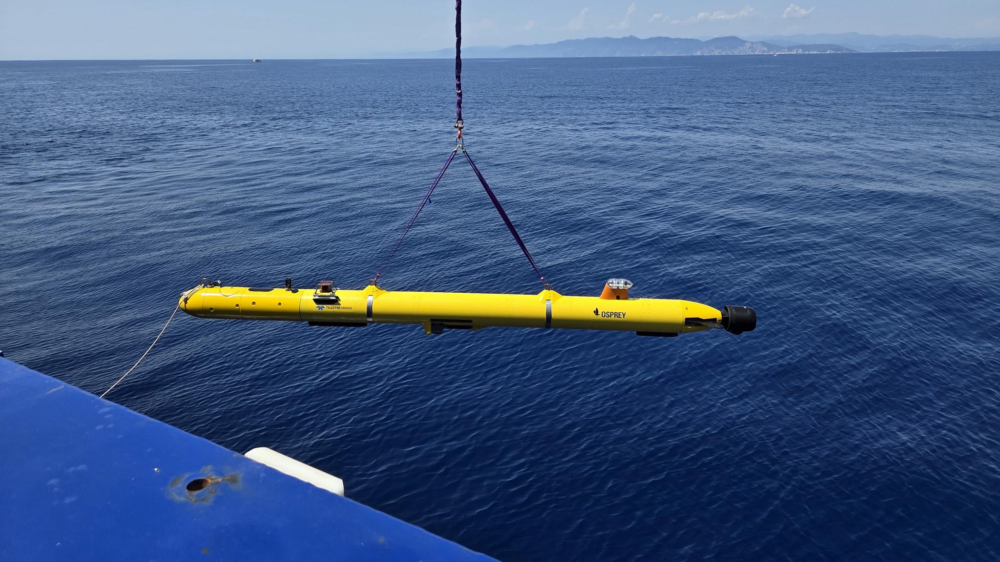 Yellow torpedo size instrument is being lifted into a blue, calm sea