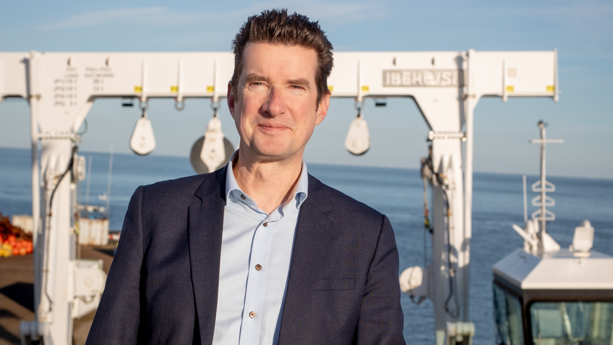 Smiling man on deck of a research vessel with large white frame and sea in the background