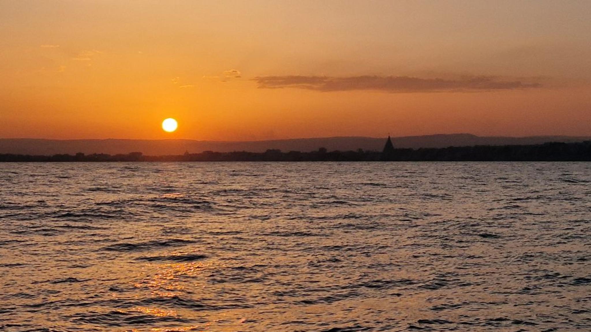 Sicily seen from the vessel, with an orange coloured sunset sky due to all the dust in the sky