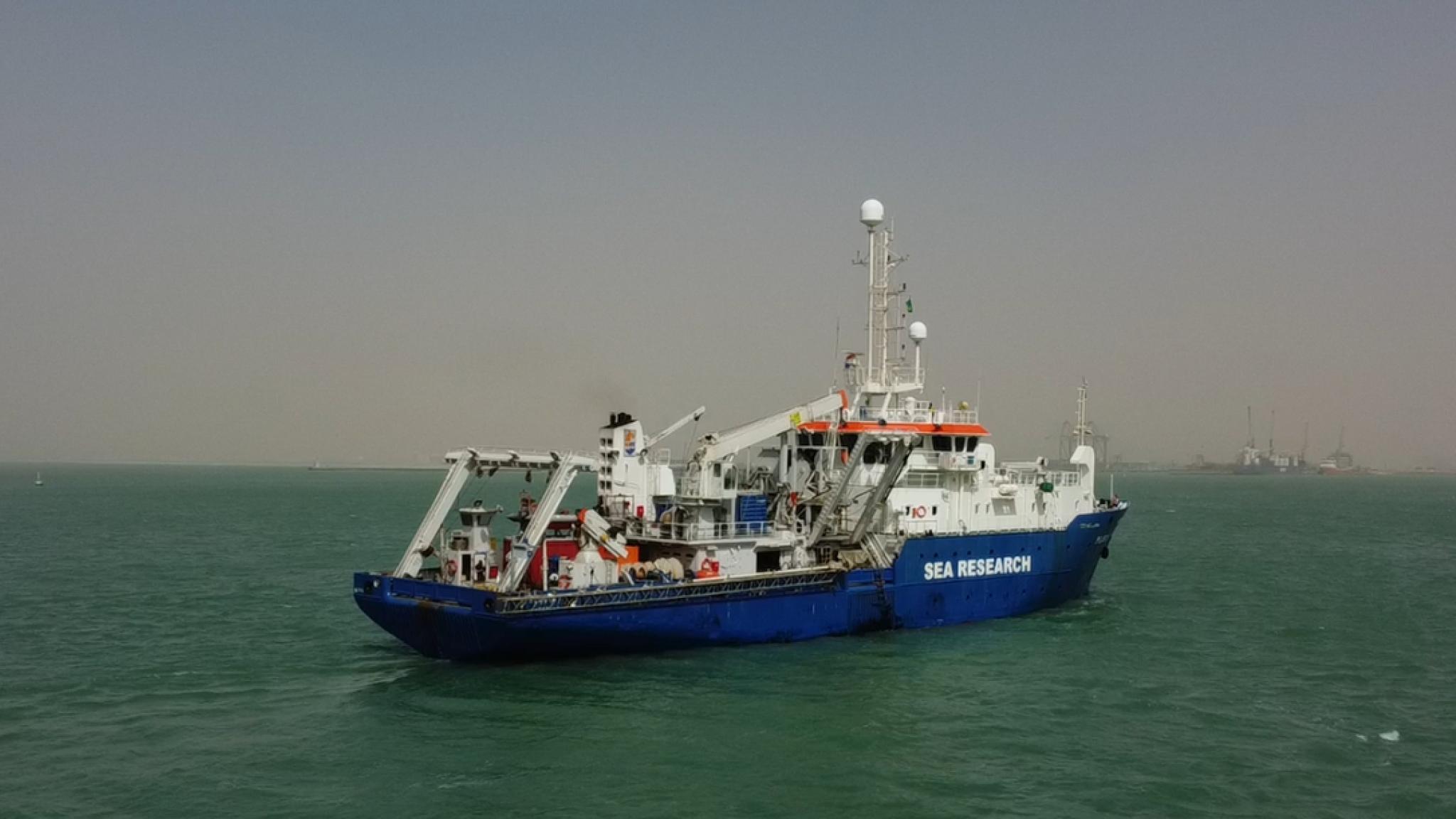 A blue-and-white research vessel labeled “SEA RESEARCH” sailing on calm green water.