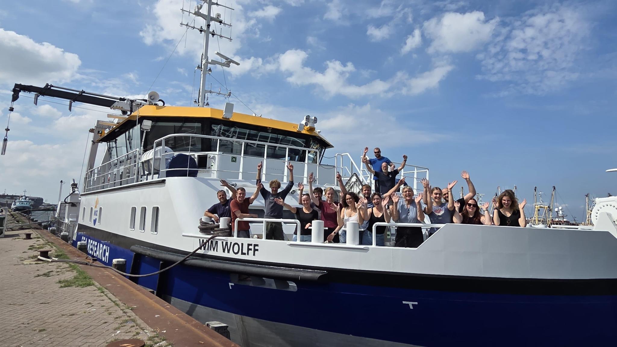 A group of people standing on the front deck of the RV Wim Wolff, cheering enthusiastically