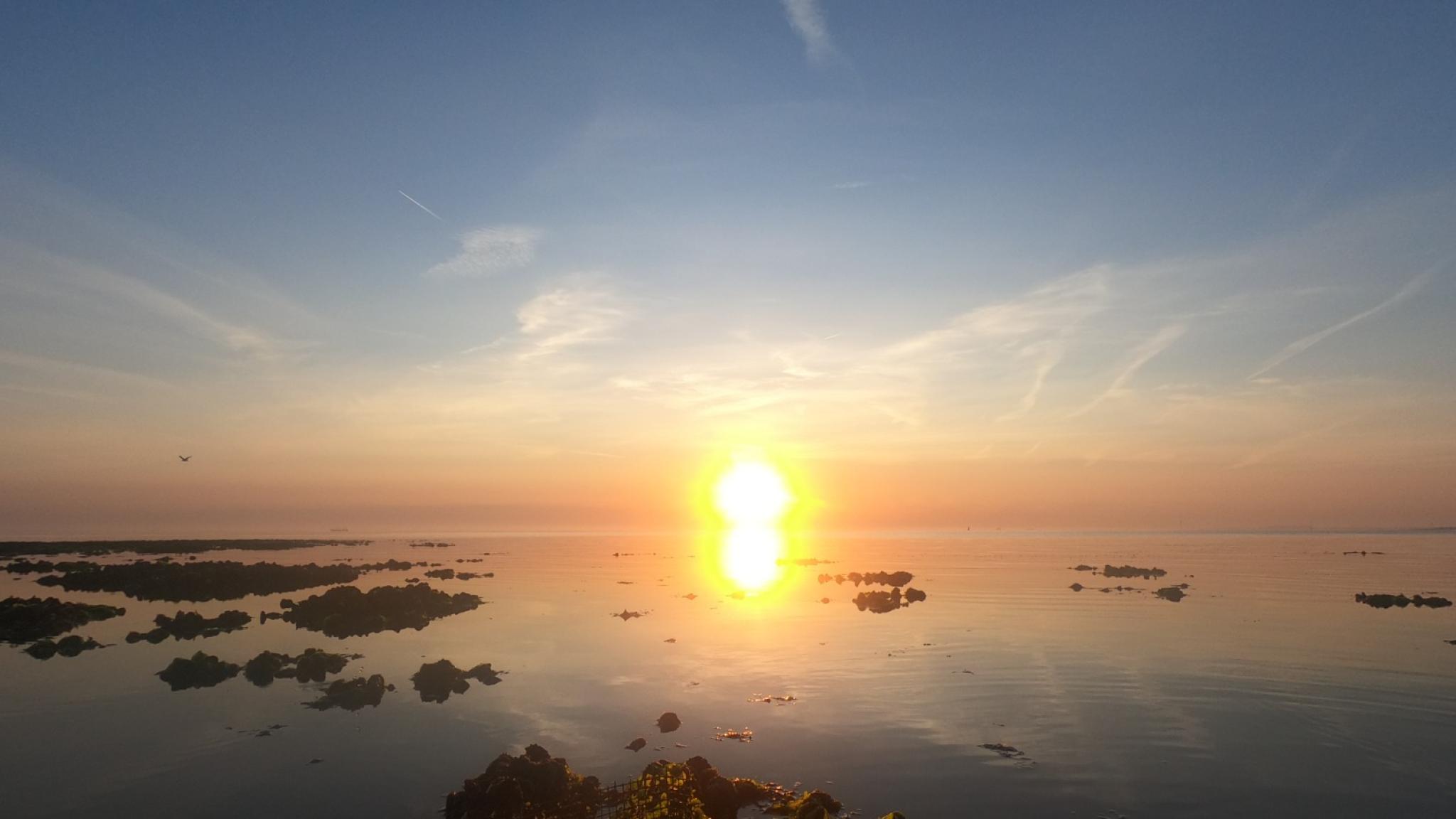 Zonsondergang boven een rustige zee met hier en daar wat rotsen in het water.