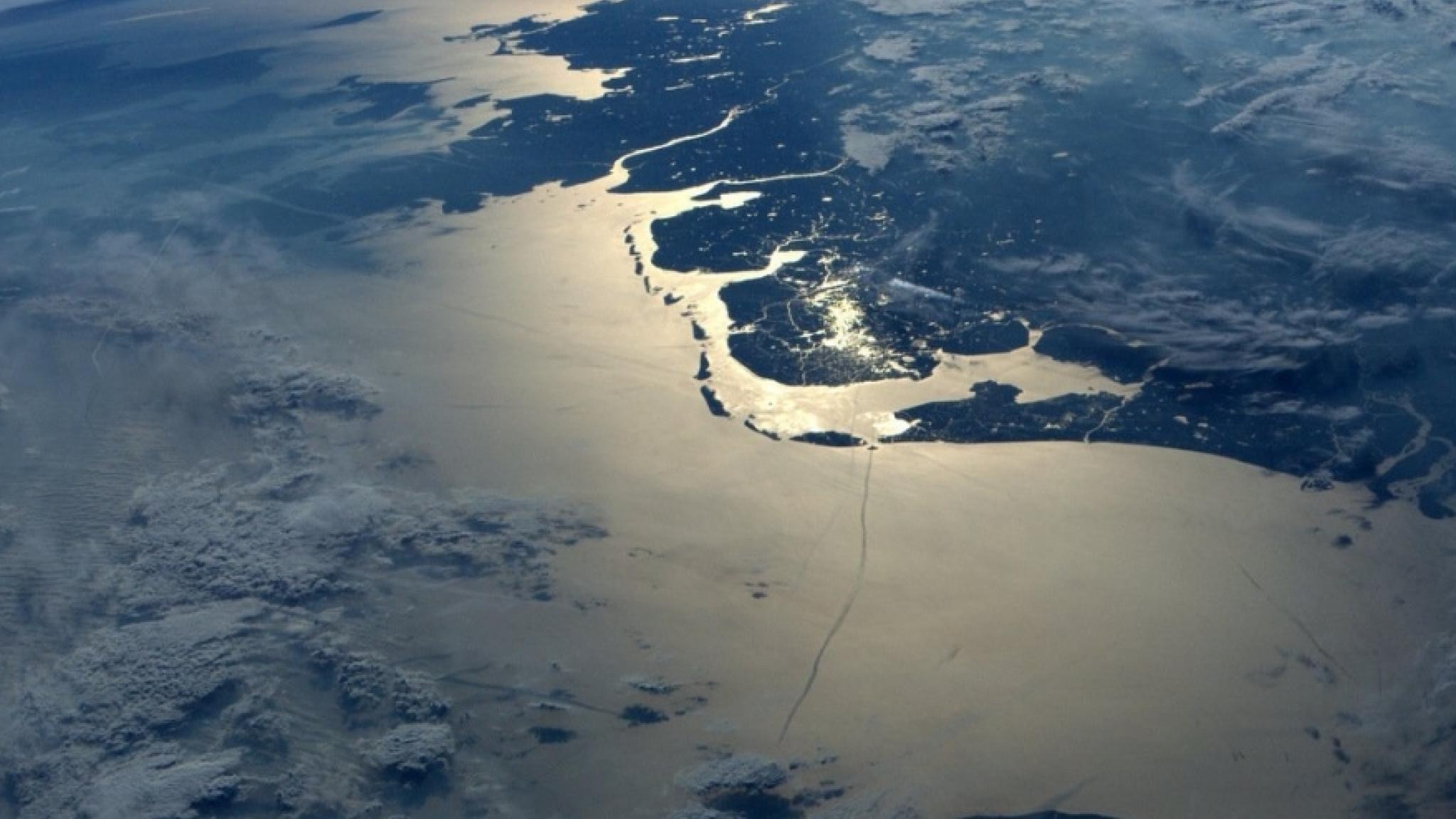 Luchtfoto van de Waddenzee met glinsterend zonlicht op het water en zichtbare eilanden en geulen.