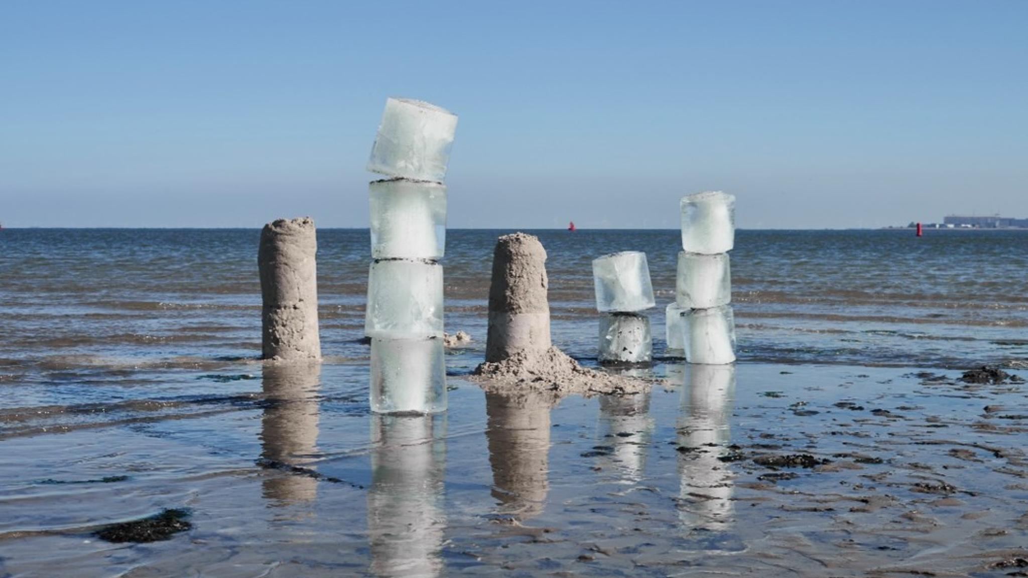Artwork installation on a mudflat, consisting of piles of large ice and sand cubes