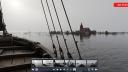 A still from a virtual reality tour. In the front there is part of a ship, as if you are standing on deck, and looking out over the water. At the horizon there is a flooded village, you see a church, some roofs of houses and some trees just above the water line. At the bottom of the screen you see different other screens showing other viewpoints in the VR tour that you can switch to.