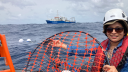 Darshika Manral sits in a zodiac at sea holding a net for deploying a Sargassum drifter, with a research vessel in the background.