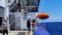 De dekbemanning van het onderzoeksschip haalt met een dekkraan een groot oranje baken uit het water Deck crew of research vessel collects large orange beacon with a deck crane 