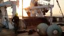 Woman with helmet walking on deck between cranes and fishing gear
