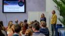 Een vrouw met een microfoon en een man staan voor een publiek