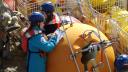 Two researchers wearing helmet and safety vests are making notes standing near a large yellow mooring