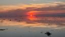 De ondergaande zon weerspiegelt zich in het rustige, ondiepe water van de Waddenzee.