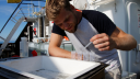 Man on research ship takes samples from a white container using a pipette