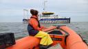 vrouw in een oranje rubberboot die koers zet naar een onderzoeksschip op de achtergrond