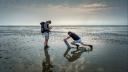 Twee onderzoekers staan op het drooggevallen wad, en nemen een bodemmonster