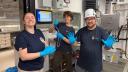 Three people wearing blue shirts and blue gloves are laughing