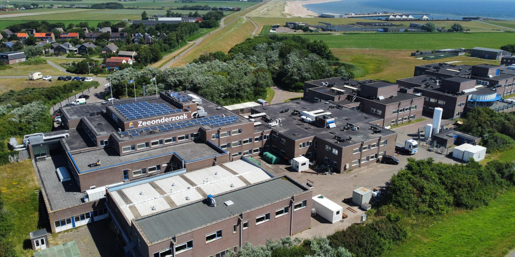 An aerial photo of the NIOZ building on Texel. You see an array of attached square buildings covered with solar panels, with a harbour in the background.