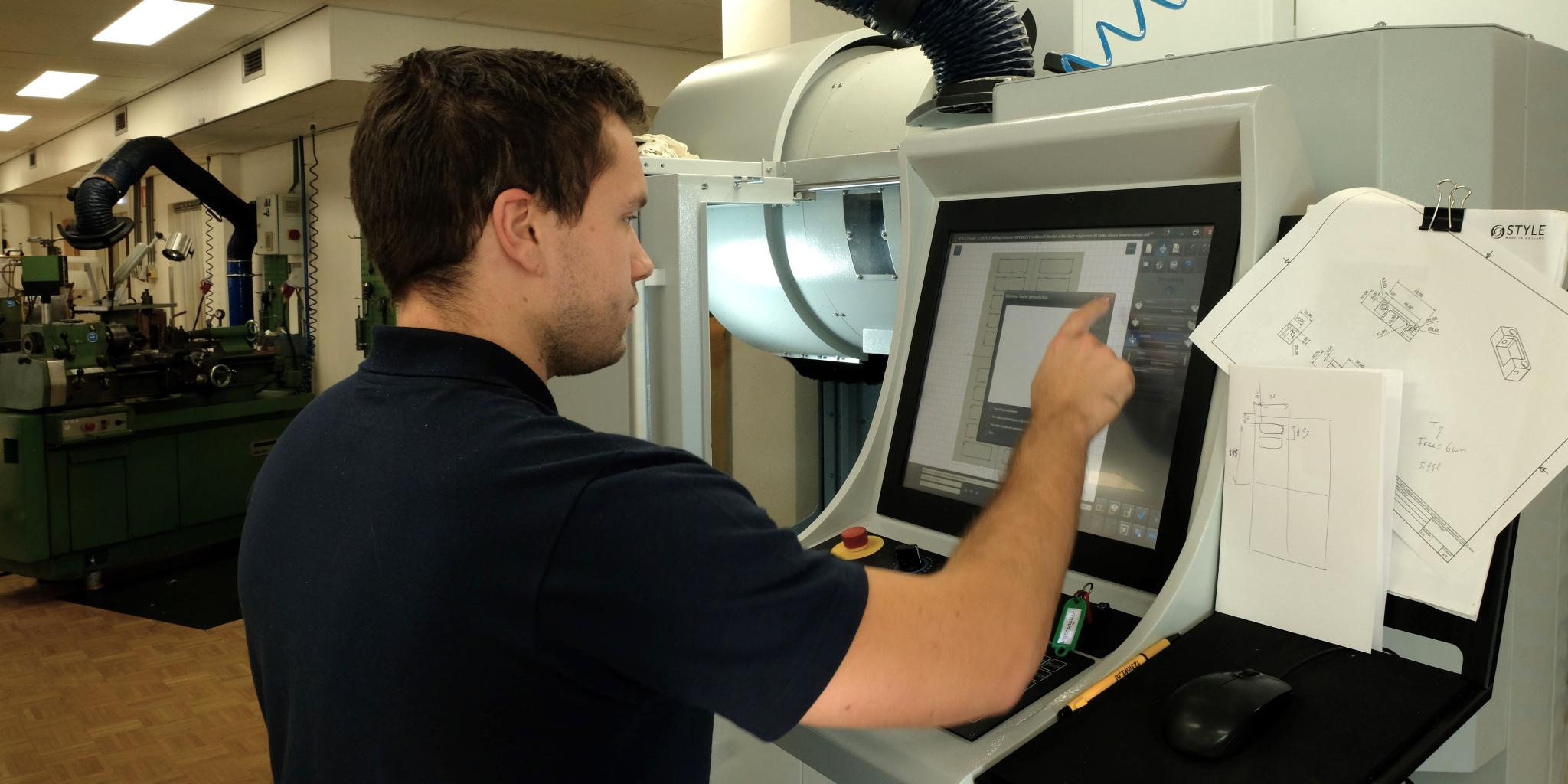 Iemand die een touchscreenpaneel gebruikt om een ​​grote freesmachine in te stellen.