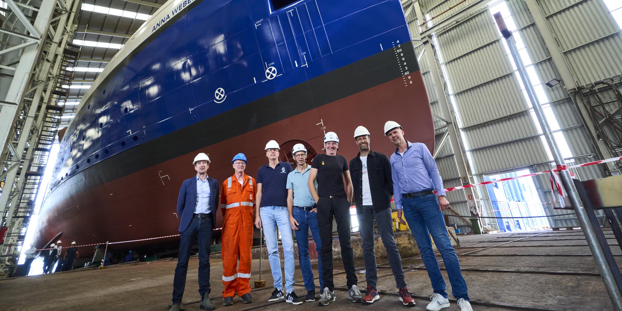 Zeven personen poseren voor een blauw schip