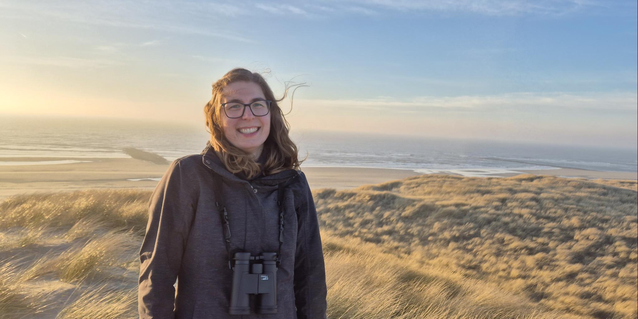 Glimlachende jonge vrouw in de duinen met zee op de achtergrond