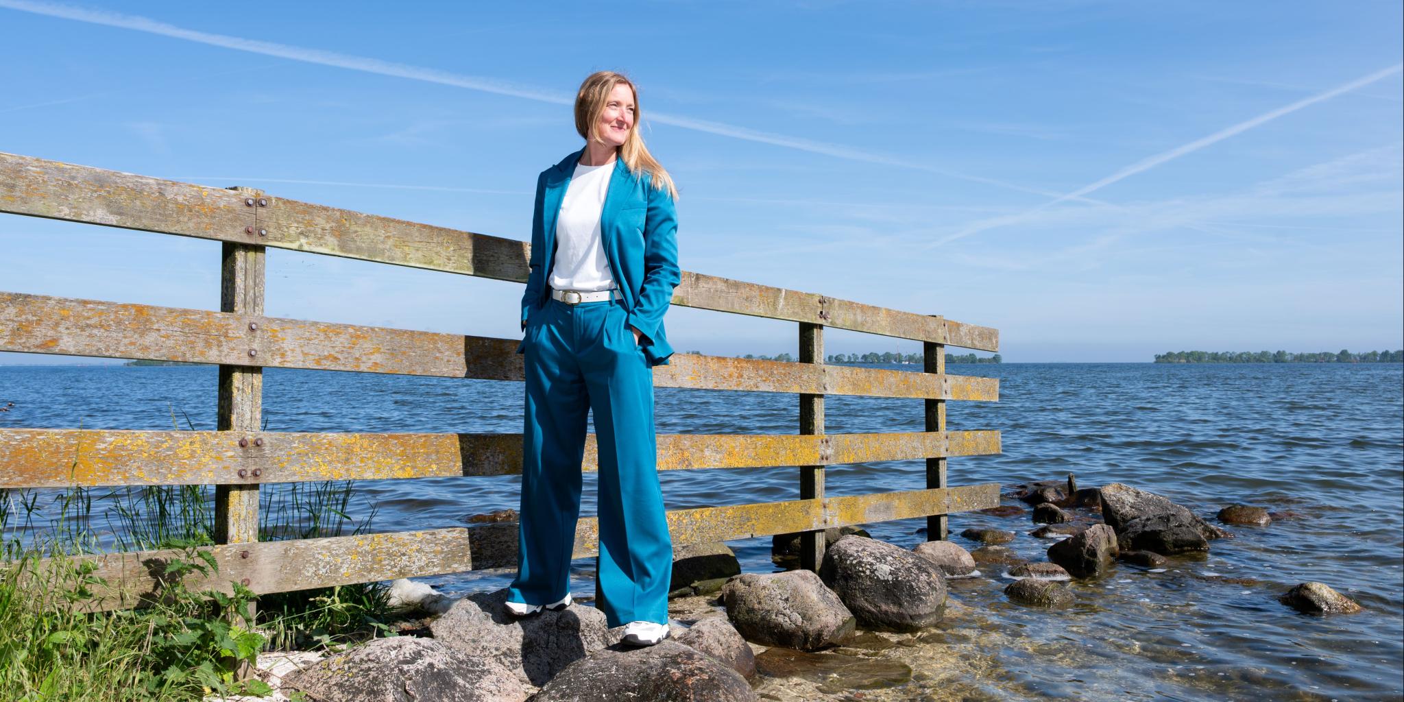 Maaike van de Kamp-Romijn staand op stenen aan de oever van een meer