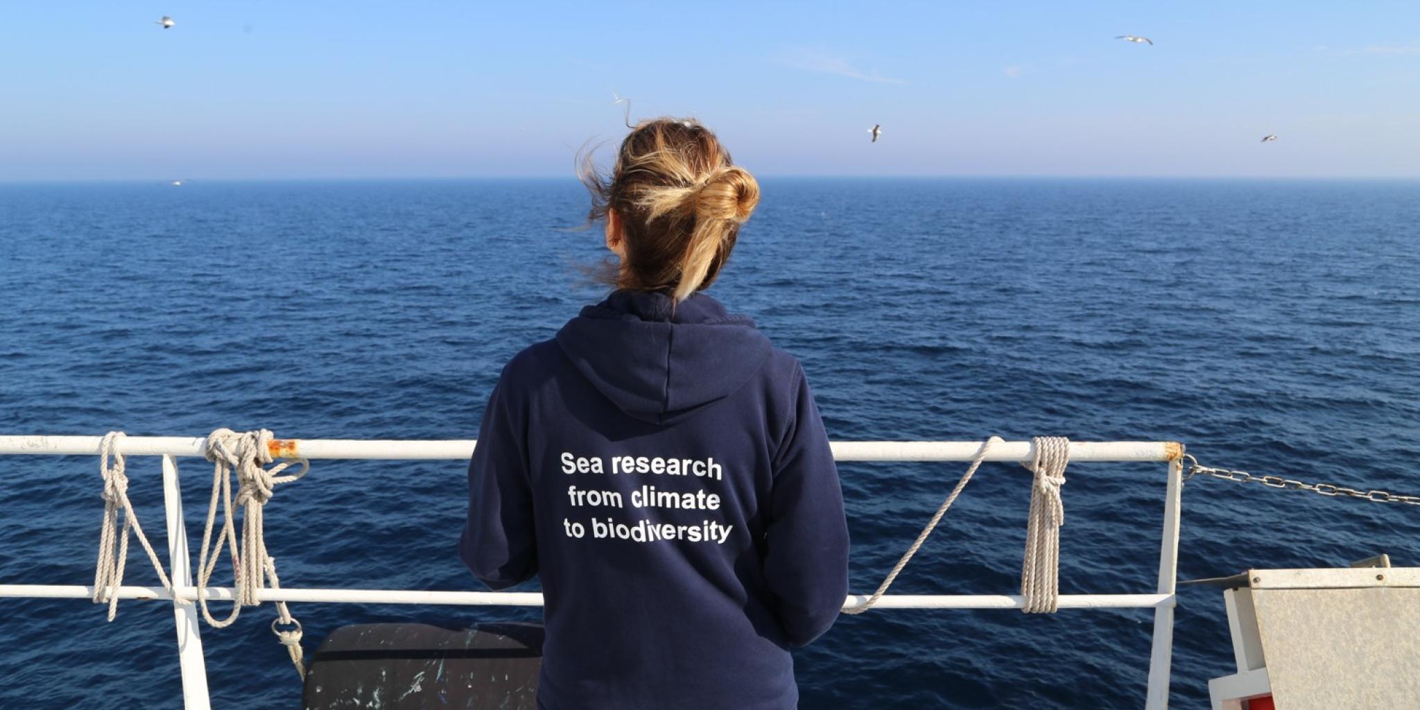 Woman seen from the back, watching the sea and holding the railing of a ship