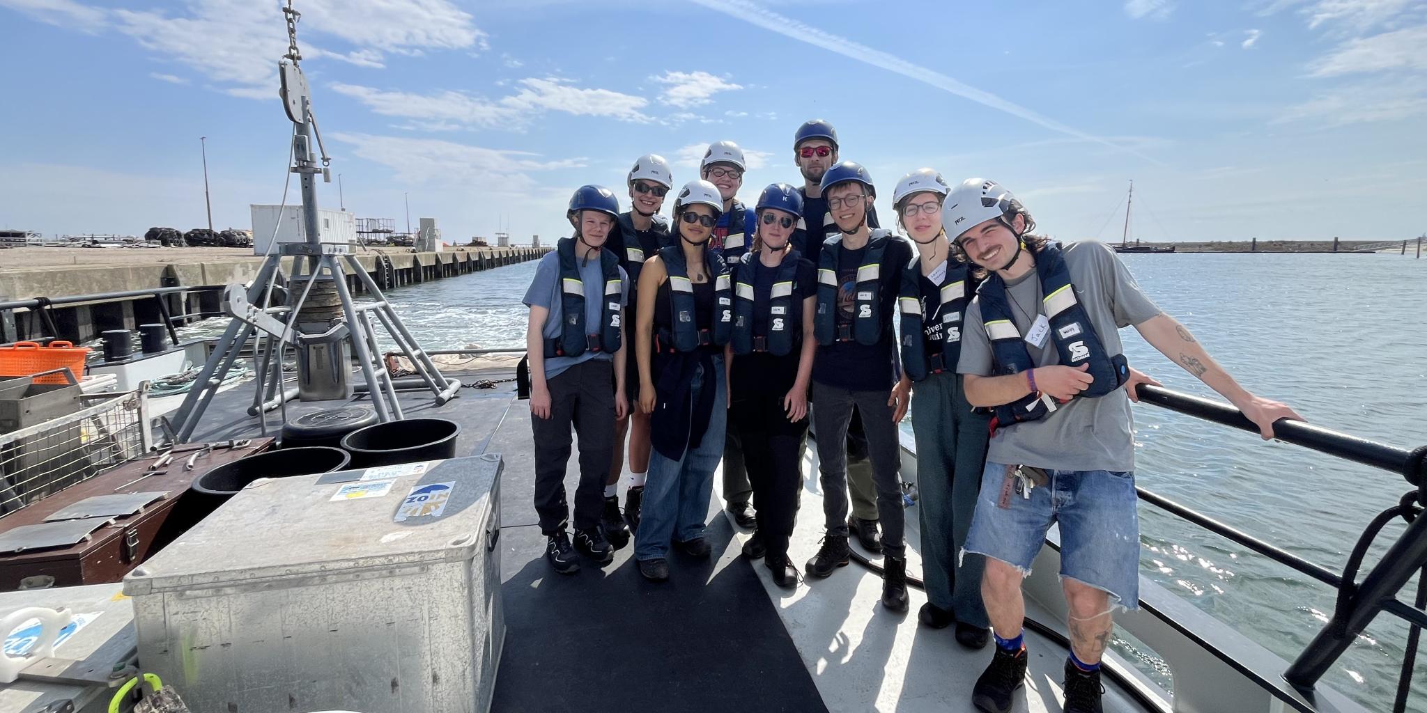 Een groep studenten in zwemvest en helm op het achterdek van onderzoekschip RV Wim Wolff.