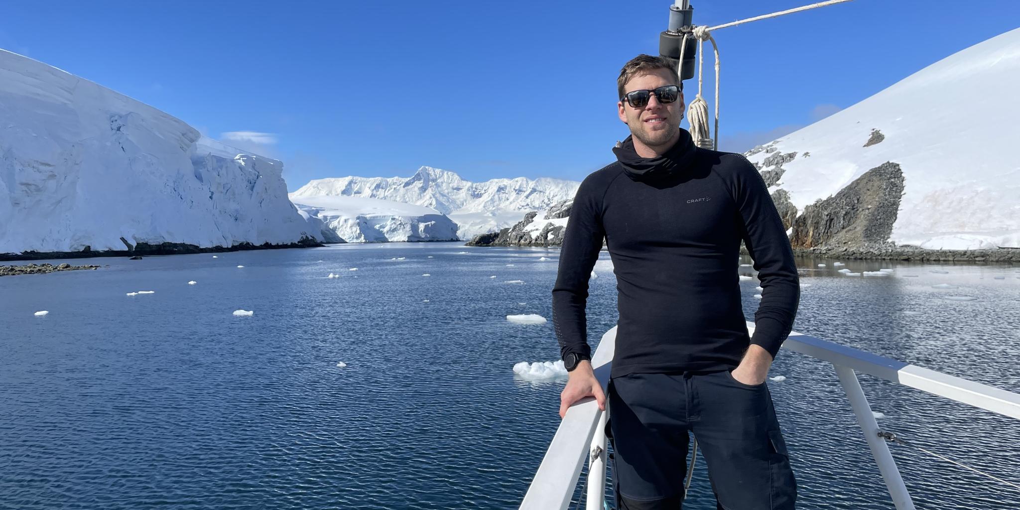 Man with sun glasses standing on a boat surrounded by icebergs