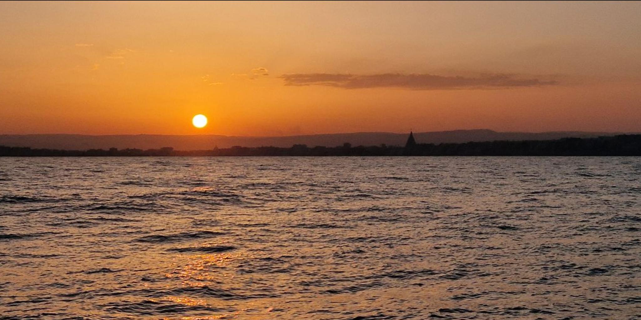 Sicilië gezien vanaf het schip, met een oranje gekleurde zonsonderganghemel door al het stof in de lucht