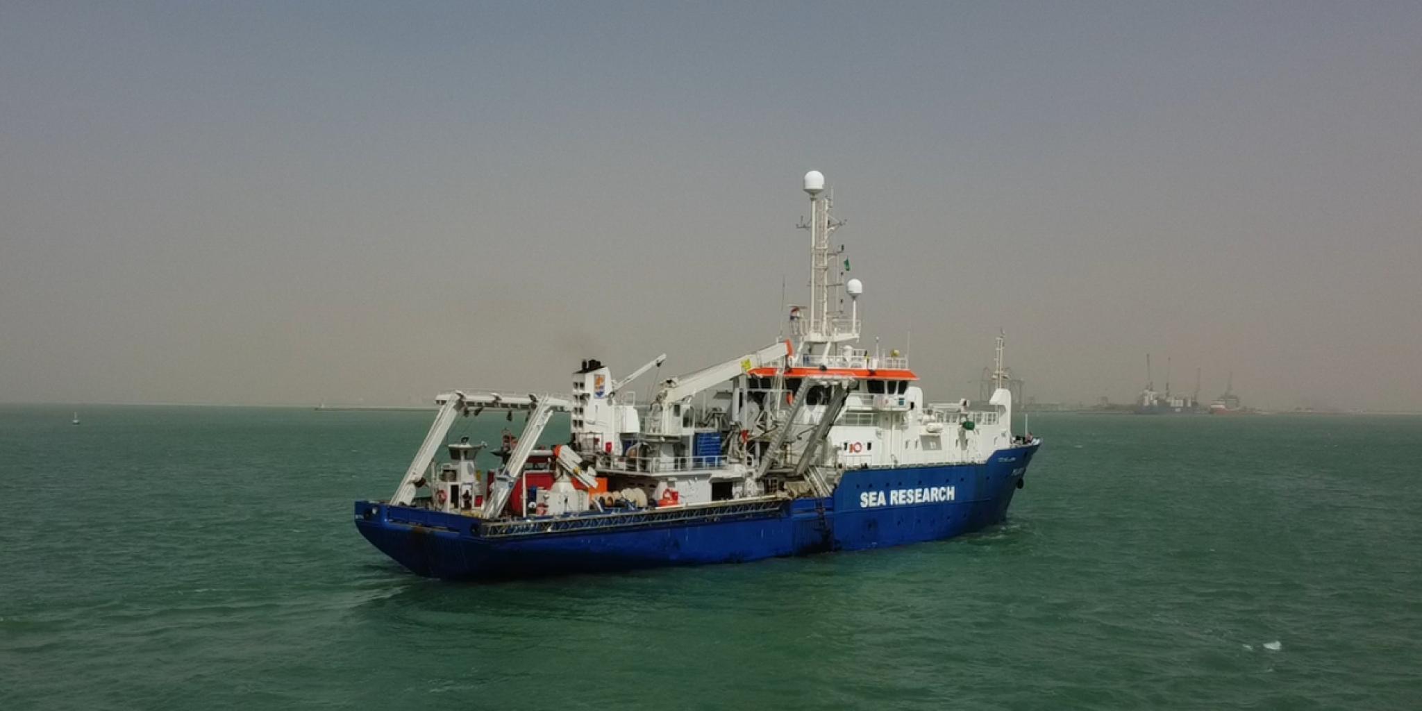 A blue-and-white research vessel labeled “SEA RESEARCH” sailing on calm green water.