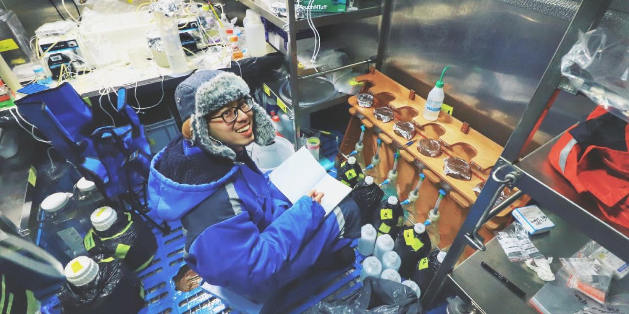 Researcher Hung-An Tian filters particulate organic carbon and nitrogen samples inside a temperature-controlled laboratory container aboard the research vessel RV Araon. Laboratory equipment, sample bottles, and filtration systems surround the workspace.