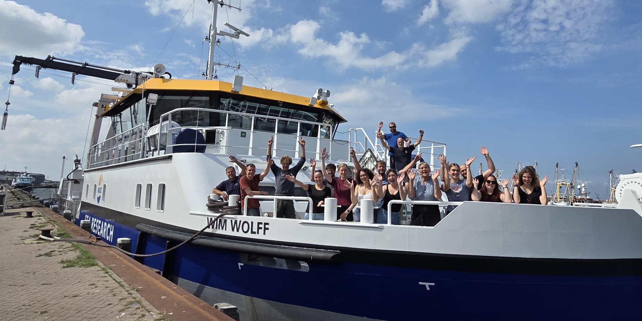 Een groep mensen staand op het voordek van de RV Wim Wolff, enthousiast juichend