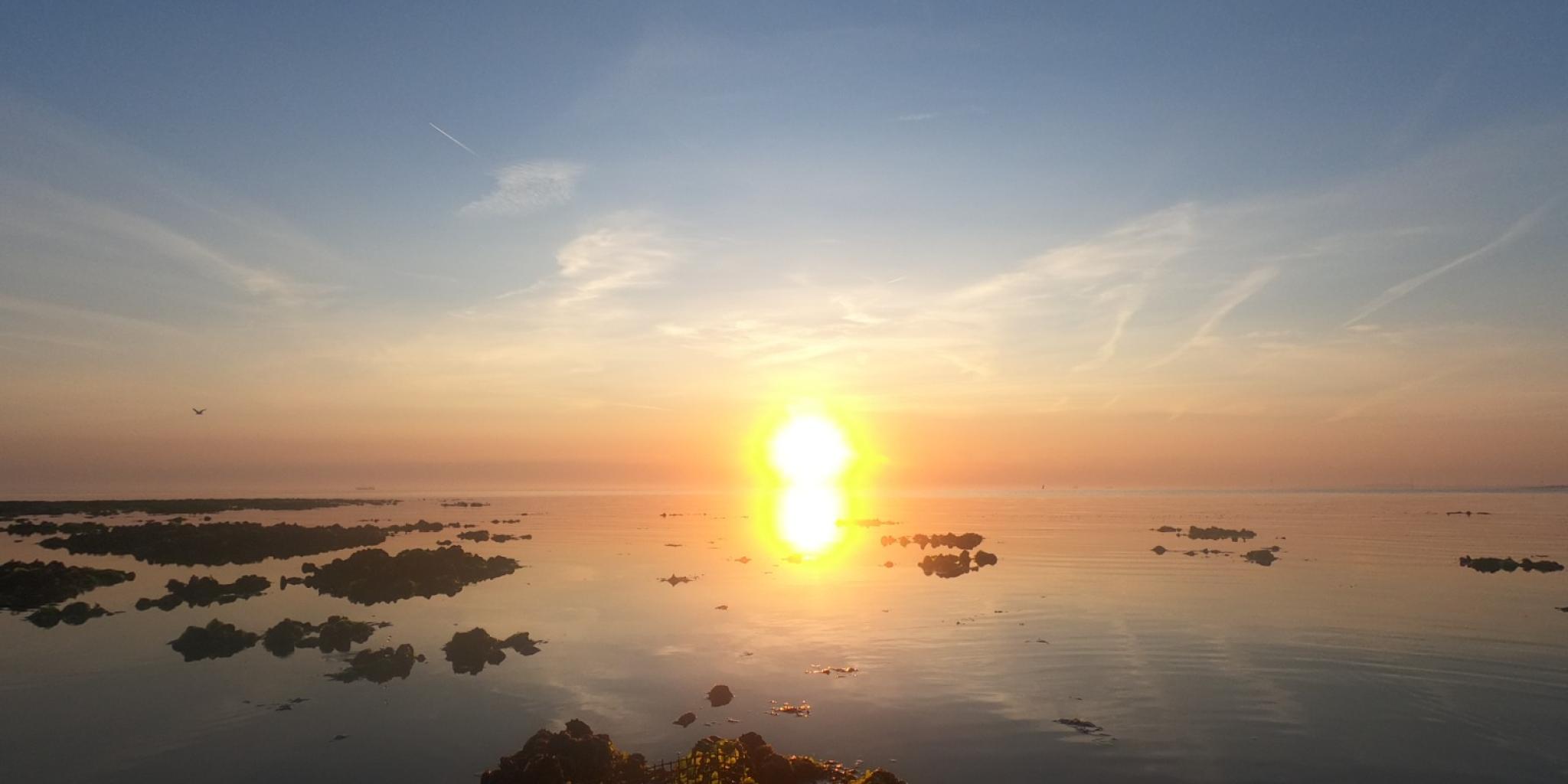 Sunset over a calm sea with scattered rocks in the water.