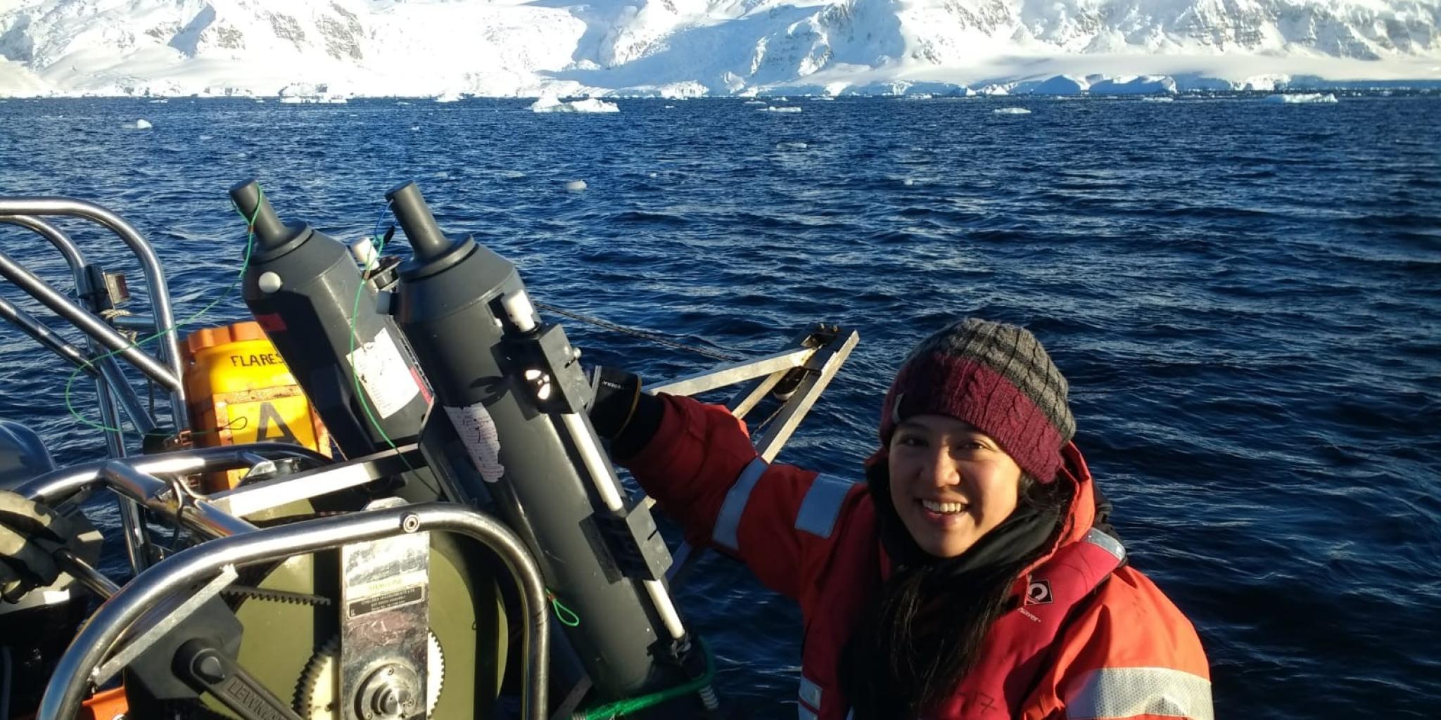 Vrouwelijke onderzoeker aan boord van een boot in Ryder Bay, westelijke Antarctische Peninsula, met besneeuwde bergen op de achtergrond.