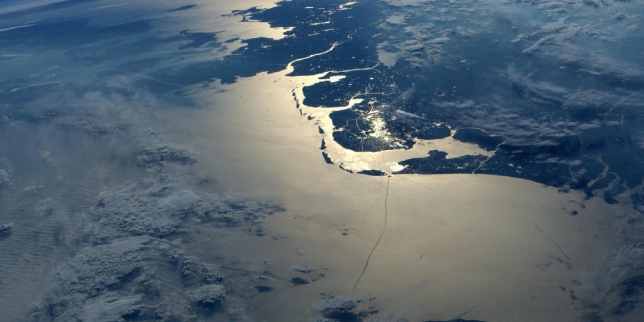 Luchtfoto van de Waddenzee met glinsterend zonlicht op het water en zichtbare eilanden en geulen.