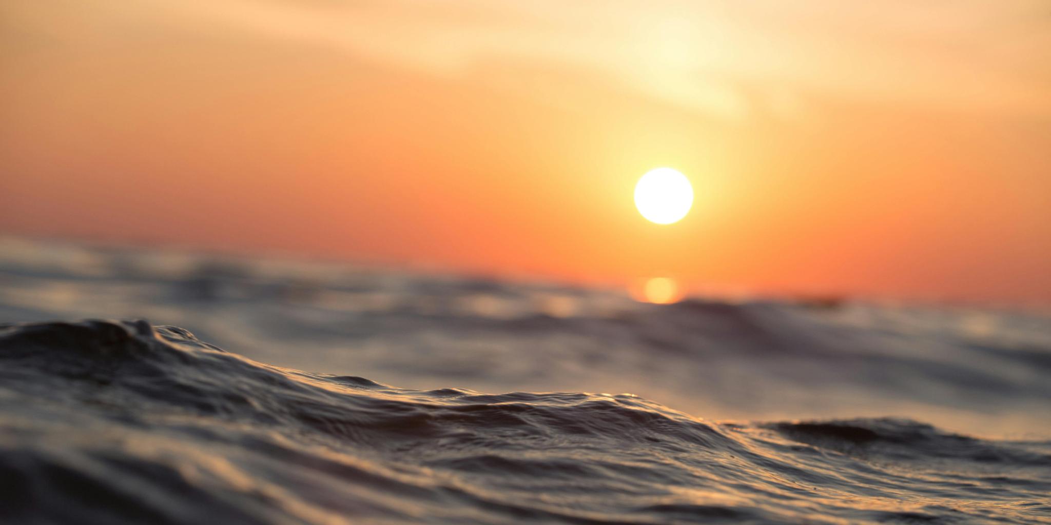 Sunset at sea in colors of orange and yellow. In front you see a water wave.