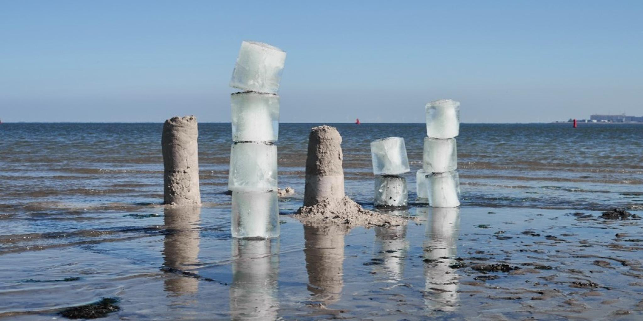 Artwork installation on a mudflat, consisting of piles of large ice and sand cubes