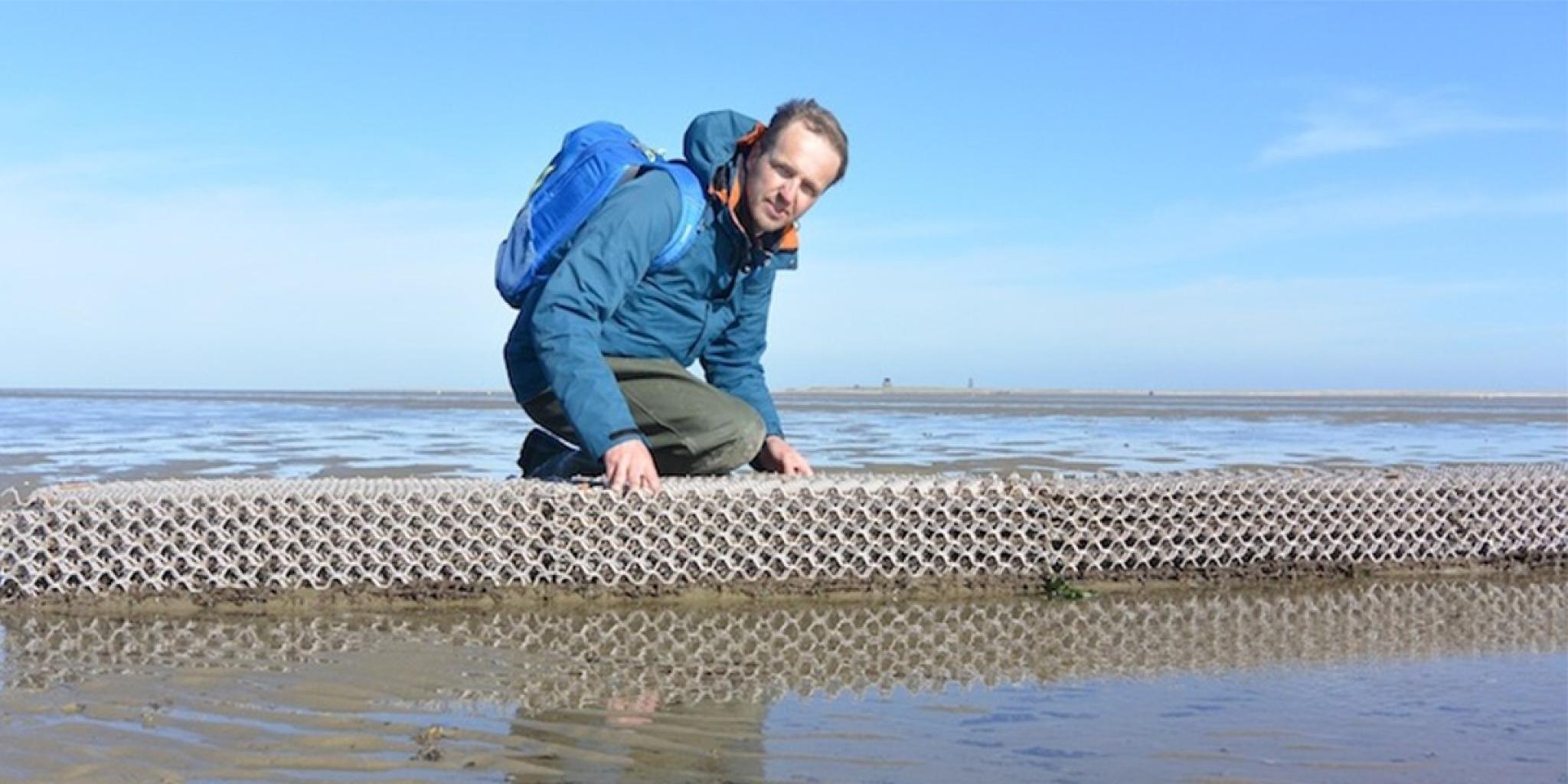 Onderzoeker knielt op een 3D-geprinte rifstructuur op een droogvallende zandplaat.
