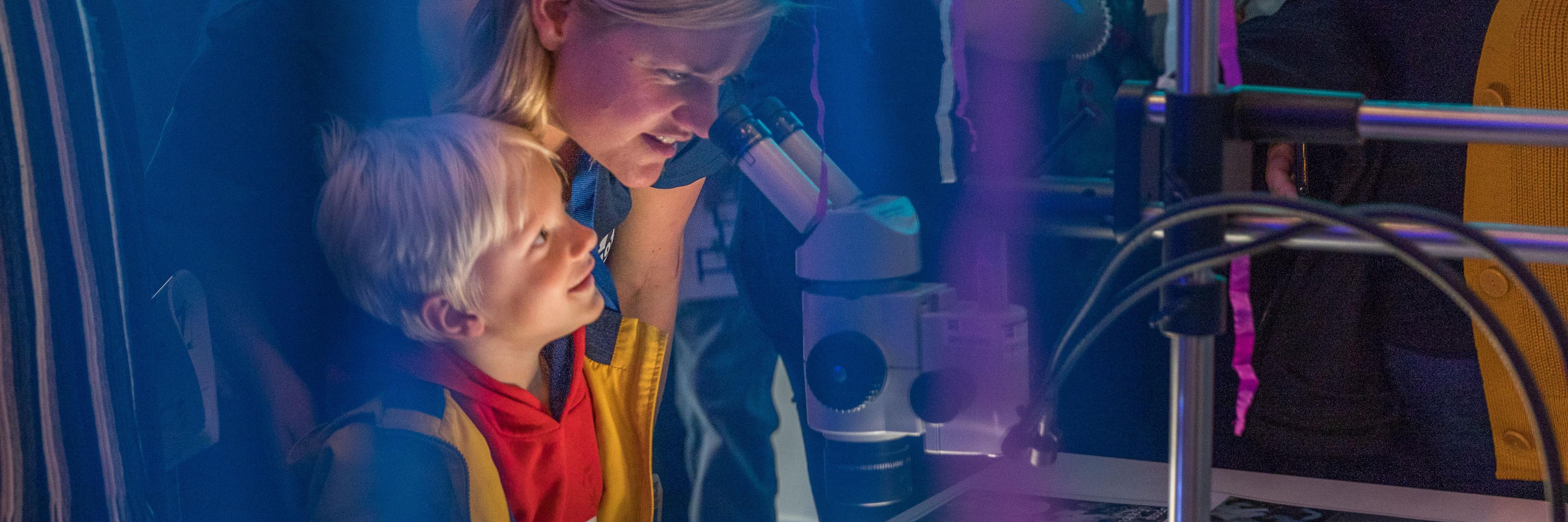 Woman and boy watch through a microscope in purple deepsea setting