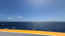 Uitzicht vanaf het dek van het onderzoeksschip Anna Weber-van Bosse over de Straat van Gibraltar, met de kust van Spanje zichtbaar aan de linkerkant en Marokko aan de rechterkant langs de horizon. De boeg van het schip is zichtbaar op de voorgrond, uitkijkend over de open zee onder een helderblauwe lucht.