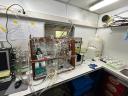 Laboratoriumopstelling aan boord van het onderzoeksschip Anna Weber-van Bosse, met glazen reactoren, slangen en meetapparatuur voor marien onderzoek.
