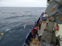 De bemanningsleden aan boord van het onderzoeksschip gebruiken een haak om de gele boei van een opgehaalde oceaanverankeringsinstallatie vast te haken, terwijl de golven langs het schip rollen.